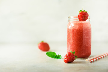 Red strawberry milkshake in glass jar on grey background with copy space. Summer food concept, vegan diet. Pink smoothie with fresh berries