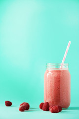 Pink raspberries milkshake in glass jar on blue background with copy space. Summer food concept, vegan diet. Pink smoothie with fresh berries
