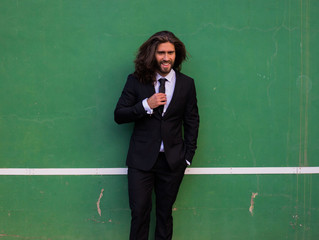 Man with long hair wearing a suit in a tennis court