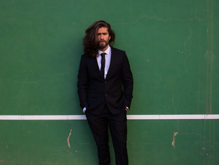 Man with long hair wearing a suit in a tennis court