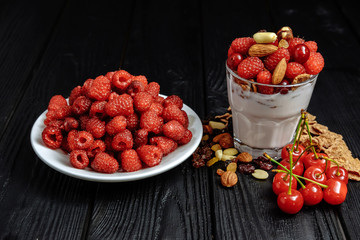 homemade yoghurt with flakes, nuts and berries of raspberries and cherries on dark wooden background