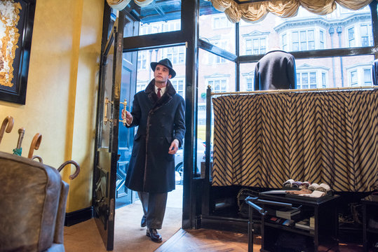 Male customer in winter coat and trilby arriving in tailors shop