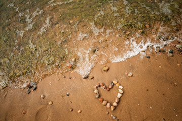 Heart shape from sea stones on a sandy ocean beach, top view, copy space. Love summer vacation background, romance concept