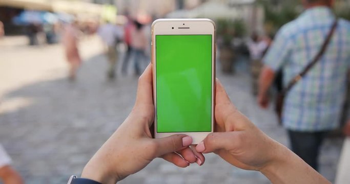 woman hand holding mobile smart phone with vertical green screen background walk people display new technology outdoor message device adult digital girl finger close up internet people slow motion