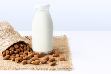 Almond milk in glass bottle with almond in sackcloth on the white table with gray background. with copy space for text.