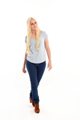 full length portrait of blonde girl wearing blue shirt and jeans, standing pose isolated on white studio background.