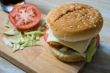 Hamburger with meat, sauce, cheese, fresh salad and tomatoes on wooden background, bread with sesame seeds