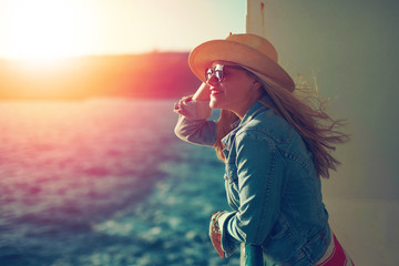 Young traveler woman on sea in hat looking away in sunset