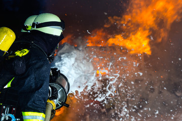 Firefighter - Firemen extinguishing a large blaze, they are standing with protective wear in front...