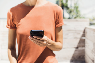 Close up of female hands using mobile phone in a city. Young woman texting on smartphone outdoor