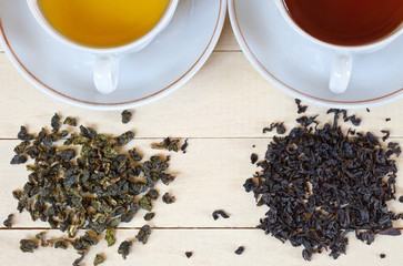 Top view of two cups with green and black tea and dried tea leaves on a wooden background....
