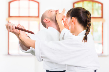 Man and woman fighting with wooden knifes at Aikido training in martial arts school 