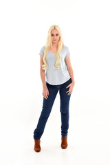 Fototapeta premium full length portrait of blonde girl wearing blue shirt and jeans, standing pose isolated on white studio background.