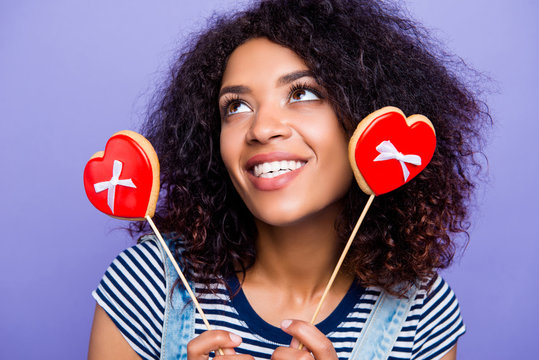 Closeup portrait of toothy positive girl having two tasty cookies in heart shape on sticks looking up isolated on vivid violent background. Fall in love concept