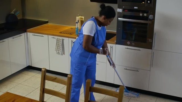 Crane shot with tilt up of black female cleaning service employee in blue uniform mopping kitchen floor