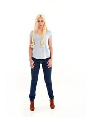 full length portrait of blonde girl wearing blue shirt and jeans, standing pose isolated on white studio background.