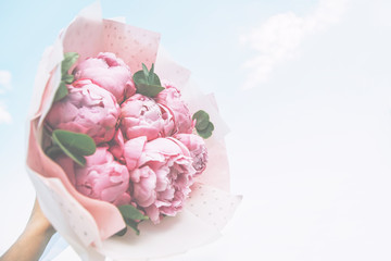 Bouquet of pink peonies in the hand sky background