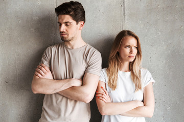 Photo of resented man and woman 20s standing together with arms folded in quarrel, isolated over concrete gray wall indoor
