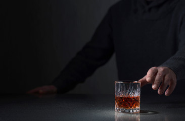 Man's hand reaches for a glass of alcohol.