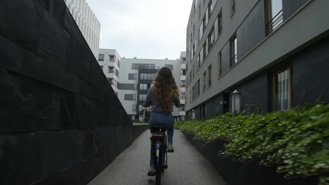 Young woman riding on bike and drinking coffee or tea. Beautiful summertime mood shot of young woman or girl riding bicycle in city. Girl with cerly hair riding on bike home. 60 fps