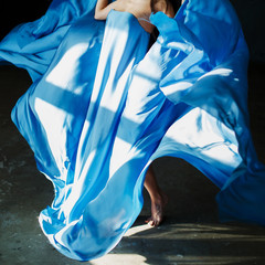  A girl in a developing blue dress is dancing barefoot on the concrete floor in the rays of the sun