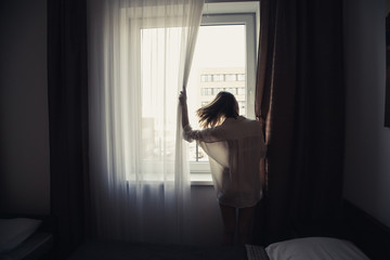 Photo of beautiful woman opening curtains and looking through the window