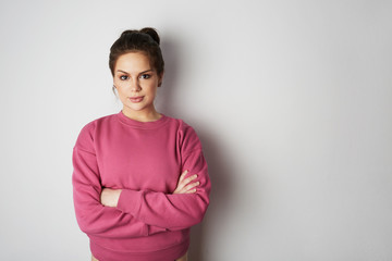 Beautiful hipster girl wearing pink hoody with space for your logo or design. Mock-up of pink hoody on white empty wall in the background. Copy paste text space