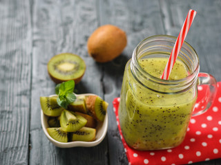 Mug with freshly made kiwi smoothie on a red rag and parsley on a rustic wooden black table.