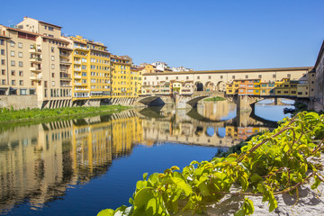 Panoramic view of the Arno River and stone medieval bridge Ponte Vecchio with beautiful reflection of colorful houses, Florence, Tuscany, Italy.
