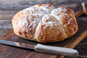 Rustikales rundes Weizenbrot und Brotmesser auf einem Holzbrett