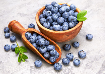 Berry blueberry in wooden dish with scoop and green leaves.