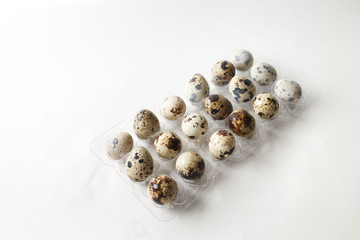 Fresh quail eggs in a plastic tray on a white background