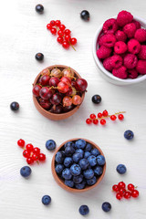 Various fresh berries close-up including blueberries, raspberries, blackberries currants and gooseberries on a white wooden background.
