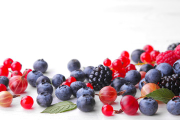 Various fresh berries close-up including blueberries, raspberries, blackberries currants and gooseberries on a white wooden background.