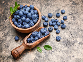 Berry blueberry in wooden dish with scoop and green leaves.