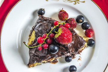 Piece of chocolate cake decorated with ripe strawberries, currant,blackcurrant top view, close up