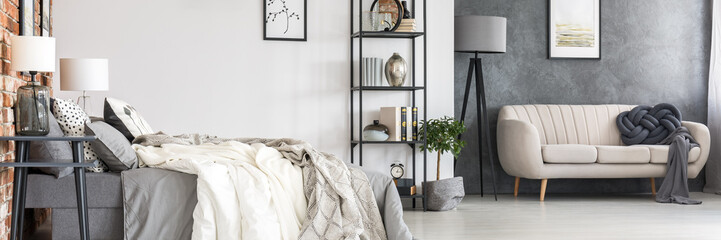 Black, industrial furniture, comfortable bed and a stylish sofa in a spacious studio sleeping and living room interior in a hipster loft with an orange brick wall - obrazy, fototapety, plakaty