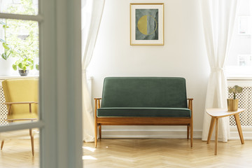 Poster above green wooden sofa in vintage living room interior with white table. Real photo