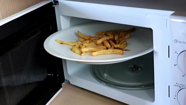 an open microwave with a white plate and roasted potatos. An large disc with french fries is wedged in a microwave oven.