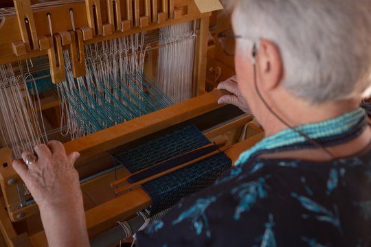 Senior woman weaving silk at shop - Powered by Adobe