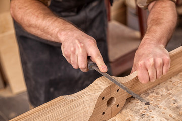 Close up of young  man builder wearing in a plaid shirt   treating a wooden product with a chisel in the workshop, close-up