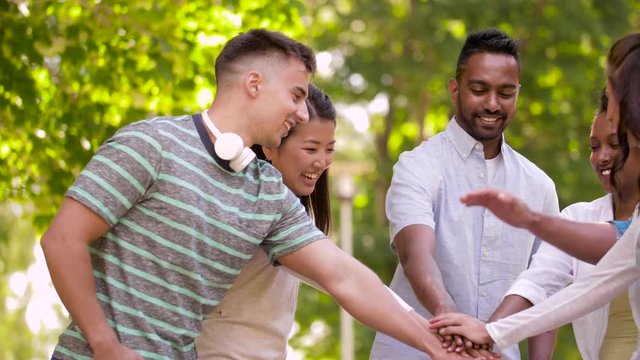 unity, friendship and international concept - group of happy smiling friends stacking hands in summer park