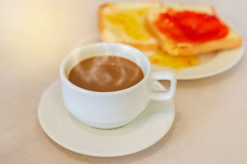 hot coffee in white cup with steam and sliced breads with marmalade jam for breakfast on table