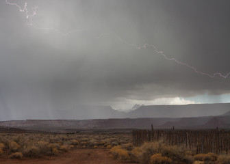 Lightning strikes in a hailstorm above Zion National park with an old cedar post corral in the foreground.