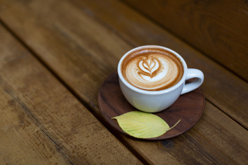 Beautiful cup of cappuccino on the wood background. A leaf on the plate gives autumn vibes. Hipster concept. Top view, flat lay