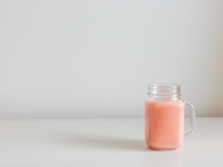 A glass jar with beautiful pink smoothie on the table. White and pastel pink colors. Minimal design. Copy-space for your text.