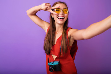 hipster photographer fashion stylish woman making photo using retro camera. Portrait on purple background.Trendy young woman with vintage film camera.wearing orange dress. Copy space.