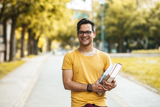 Young male student standing at the college yard.He holding a book and looking at camera.