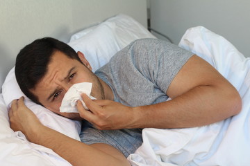 Man blowing his nose in bed 