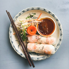 Asian style dinner. Flat-lay of summer rice paper rolls with shrimp and teriyaki sauce in bowl over blue table, top view, copy space, square crop. Chinese cuisine © sonyakamoz